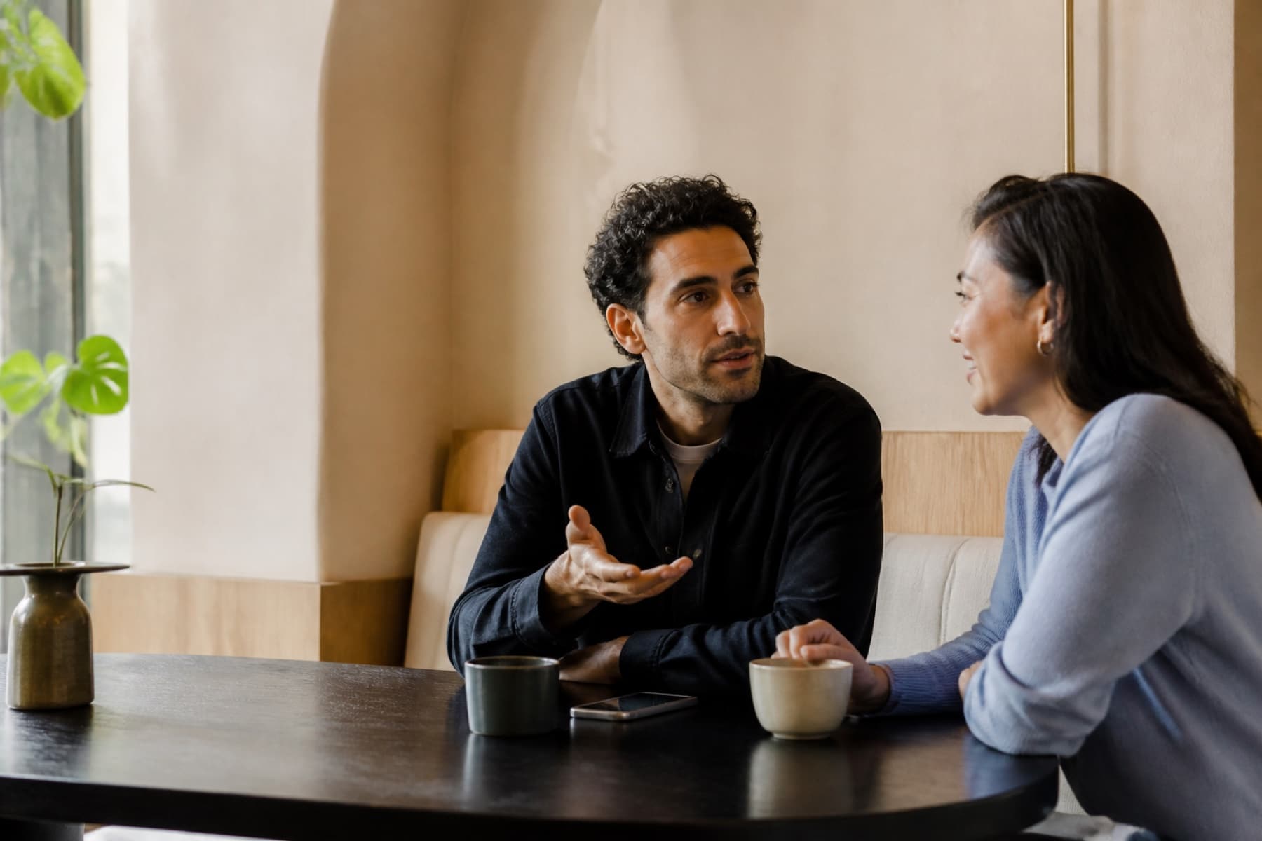 Two people talking over coffee at a sunlit European café